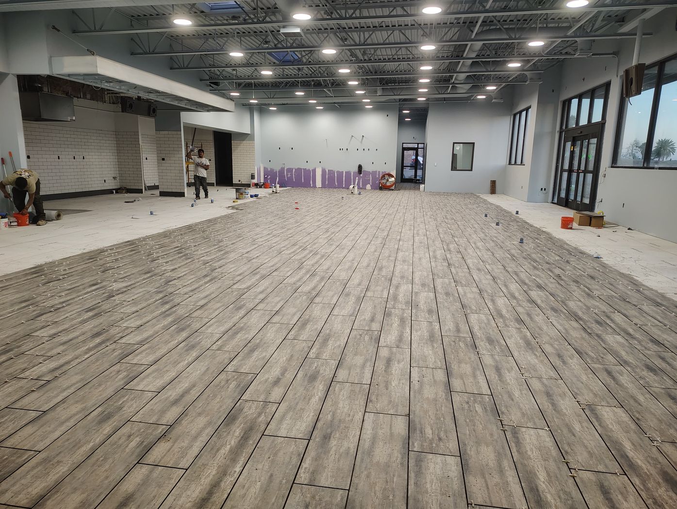 Wood-look plank tile being laid across a large open-plan floor